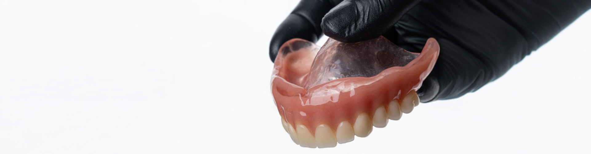 Close-up of a dentist holding a full upper denture, showing realistic artificial teeth and a pink acrylic gum base.